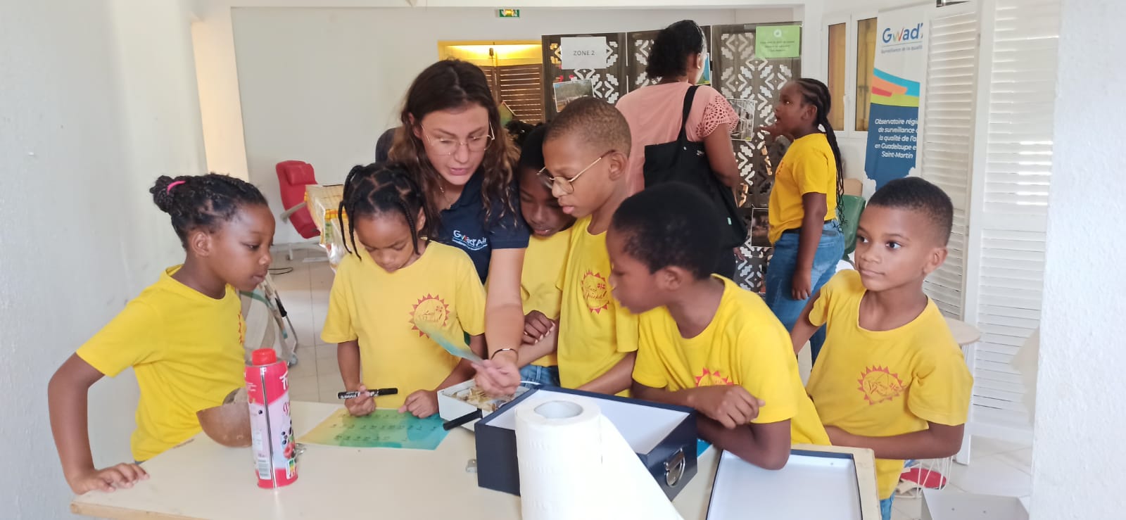 Groupe d'élèves de CE2 accompagné par une professionnelle de Gwad'Air dans la résolution d'une énigme